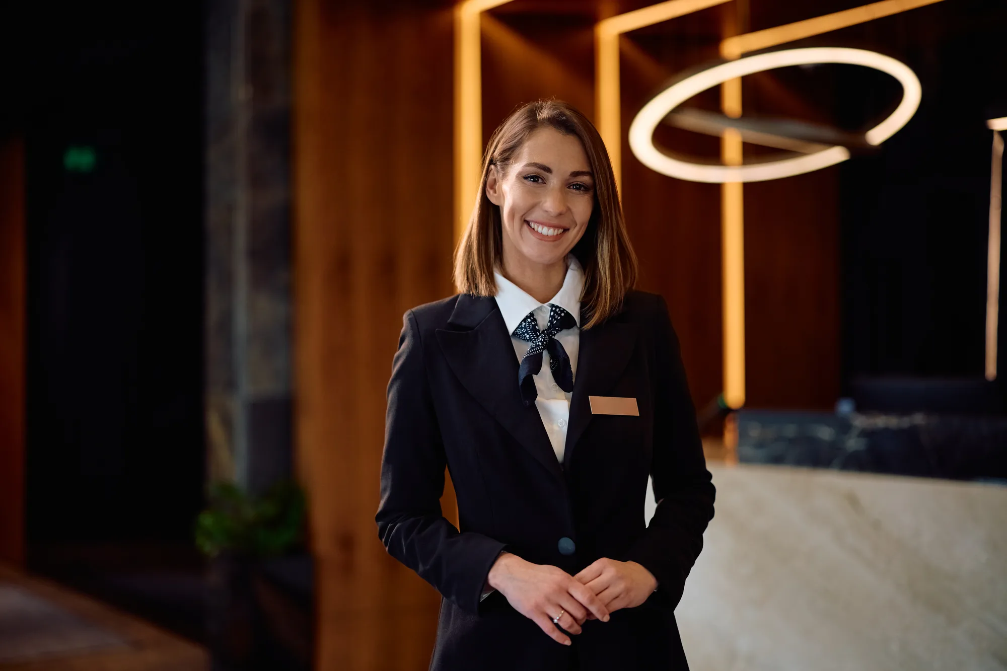 Lächelnde Hotelangestellte in Uniform steht in modernem Hotelfoyer, eine professionelle Website beginnt mit starkem ersten Eindruck