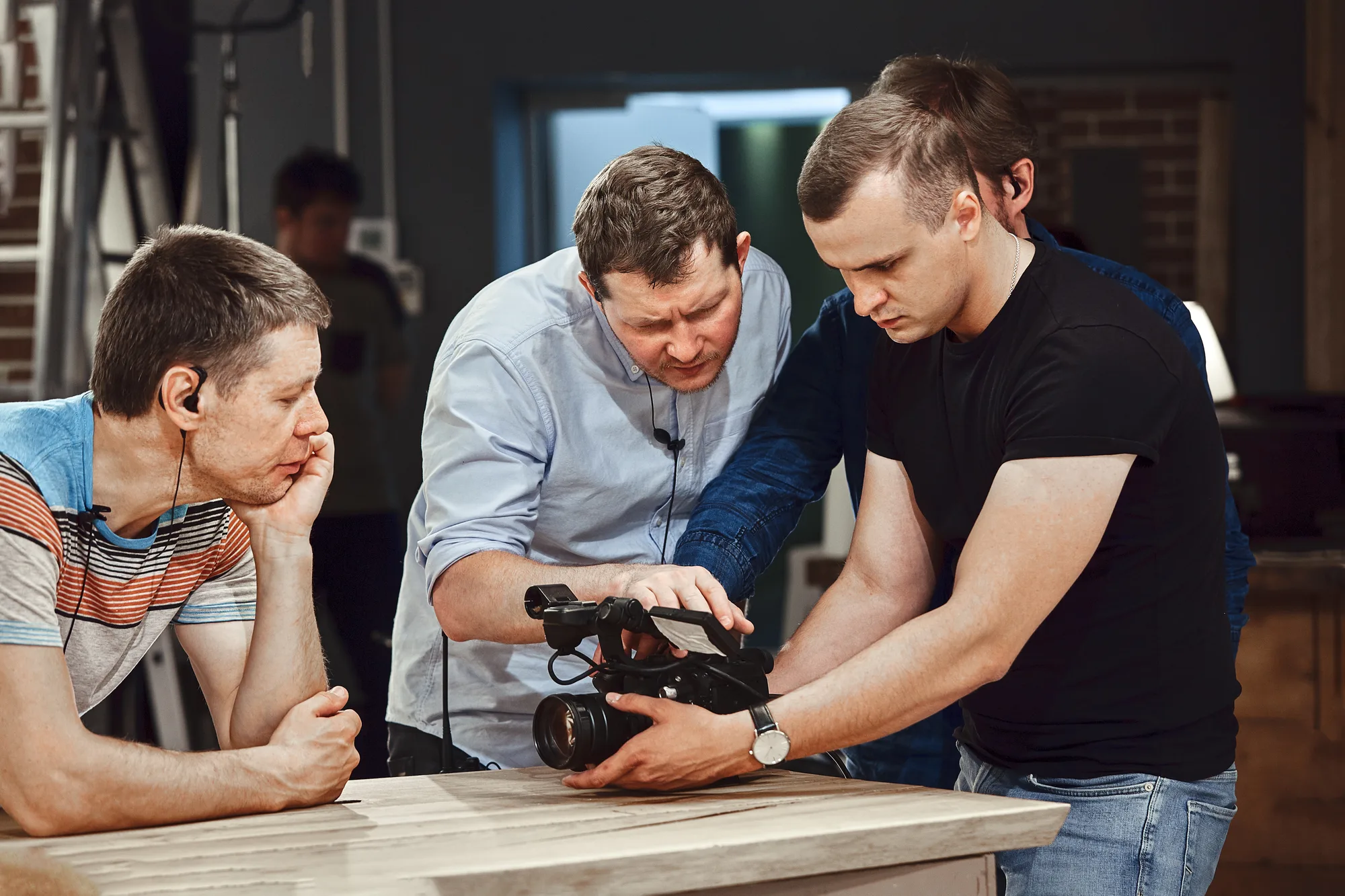 Drei Männer begutachten gemeinsam eine professionelle Videokamera im Filmstudio