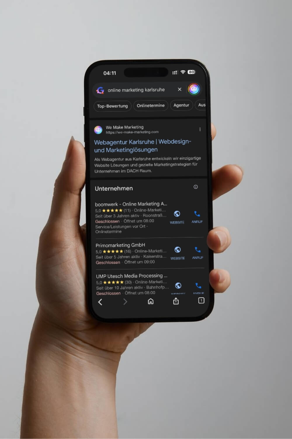 Hand hält Smartphone mit Google-Suchergebnissen zu Online Marketing in Karlsruhe, inklusive Webagentur-Listing.