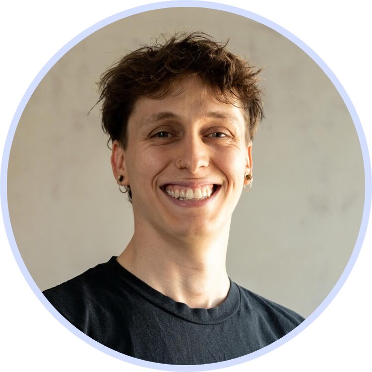 Smiling person in a studio-style headshot with short hair and earrings against a neutral background.